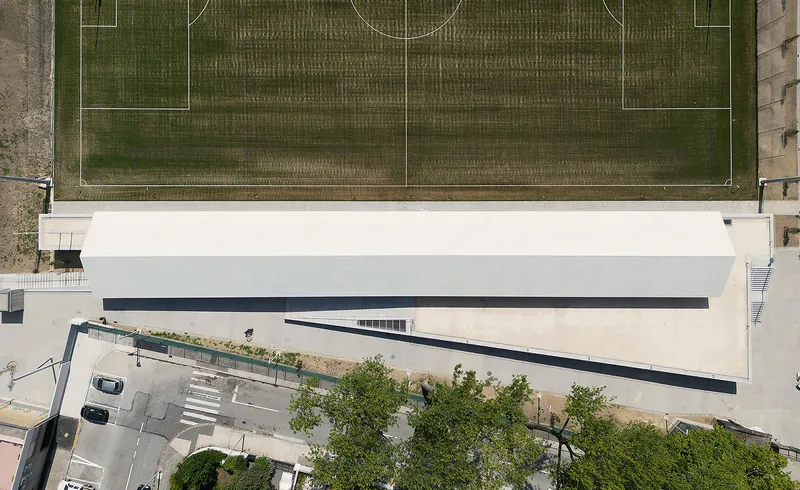 Overhead view showing the long rectangular roof plane parallel to the striped sports pitch below