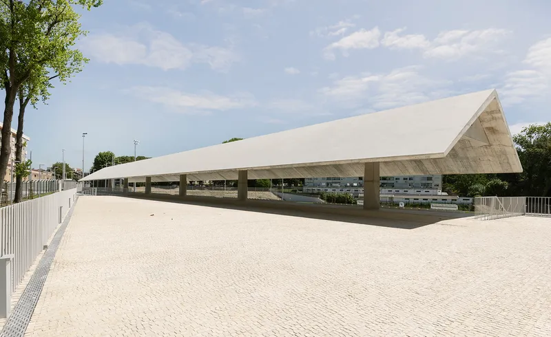 Cantilevered roof over the stadium seating area with paved plaza and trees under afternoon sun