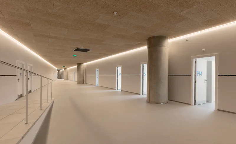 Interior concourse with continuous perimeter lighting along the board-marked concrete ceiling and circular columns