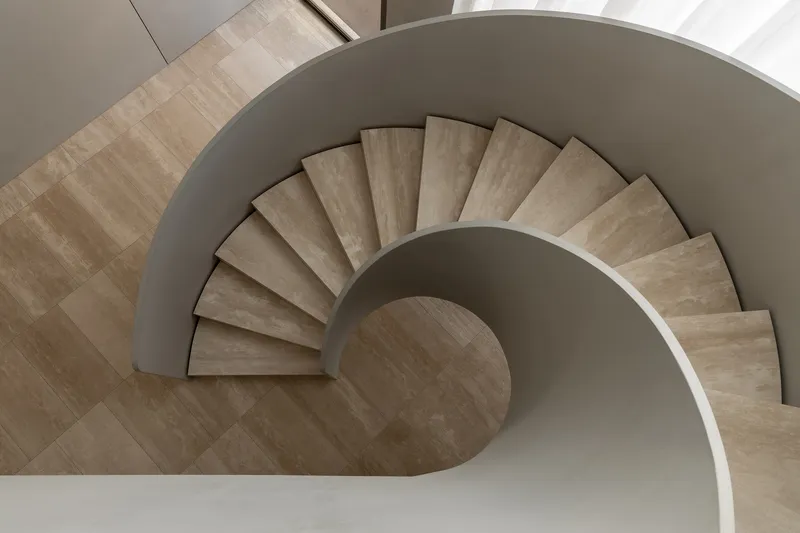 Top-down view of spiral staircase with travertine treads and curved white balustrade