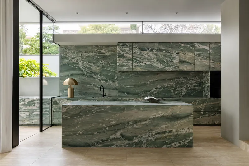 Green veined marble kitchen island and backsplash opening onto a planted courtyard through glazed doors