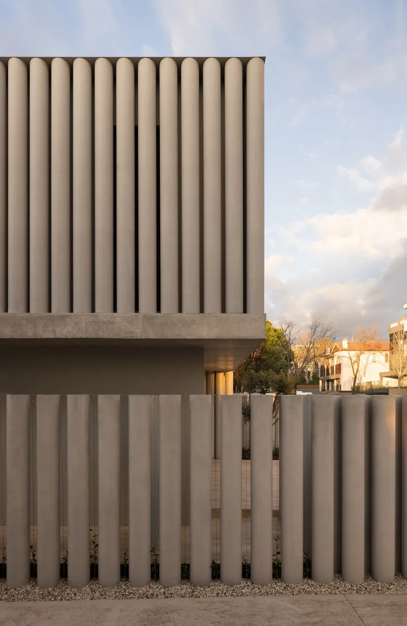 Street view of ribbed concrete facade with vertical fins above matching perimeter wall at dusk
