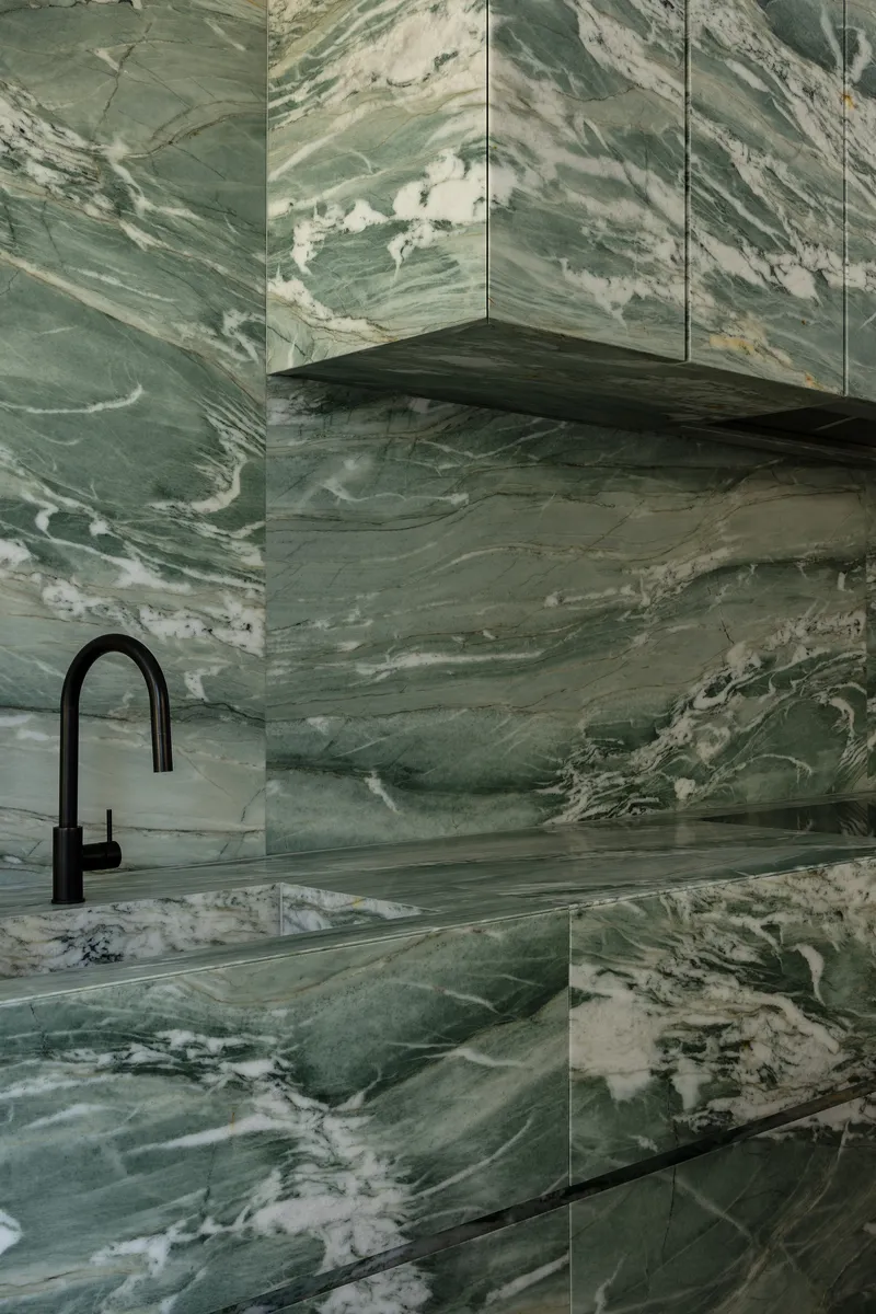 Black gooseneck tap against green and white swirled marble walls and countertop in close-up
