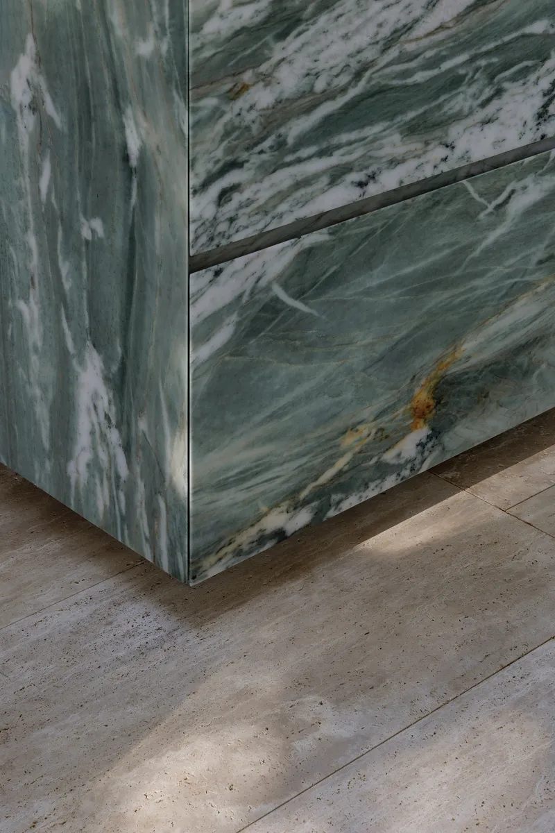 Corner detail of veined green marble panels meeting a travertine floor
