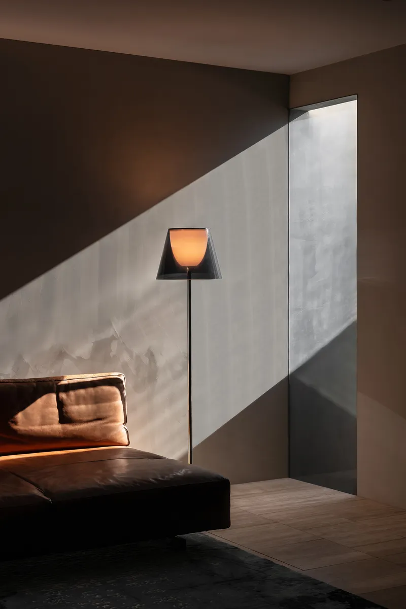 Floor lamp casting triangular shadow across textured wall and upholstered bed corner