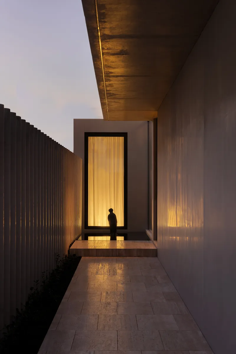 Entry corridor with vertical timber slat screen and backlit doorway at twilight