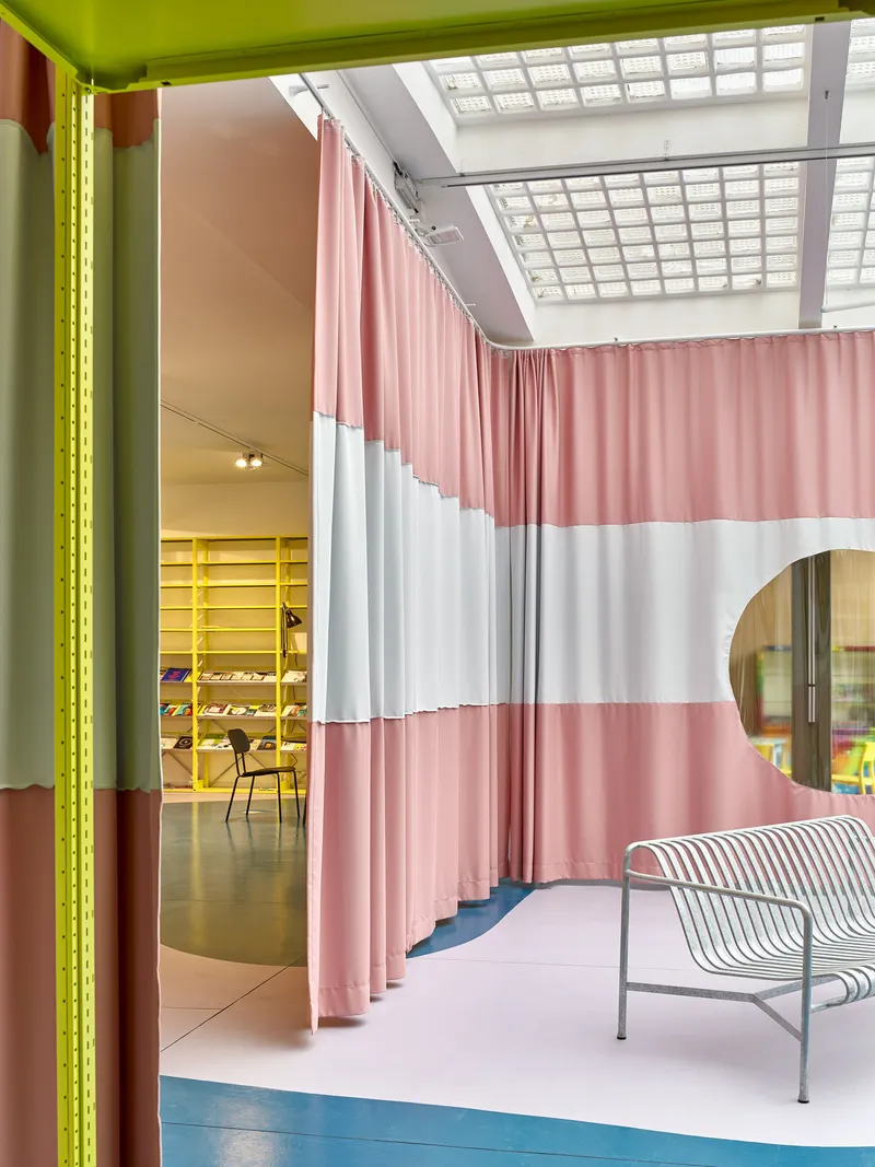 Corner view of striped curtain divider with skylight above and wire bench on blue floor