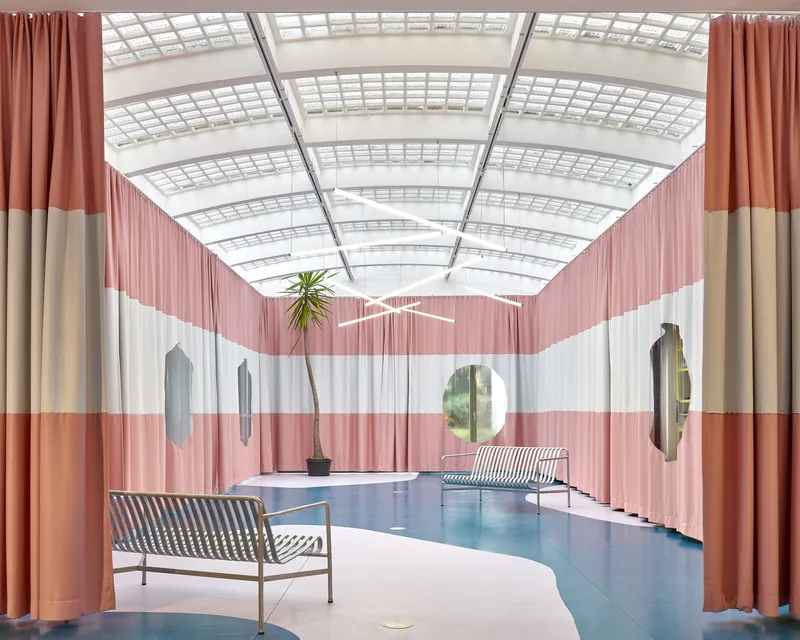 Lengthwise view through hall with striped benches on curved blue floor under gridded skylight