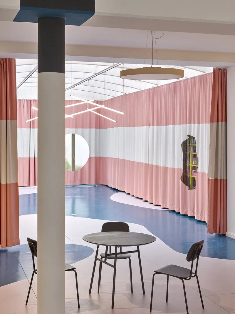 Interior with striped pink curtain partitions and round table beneath a coffered skylight and suspended ring light