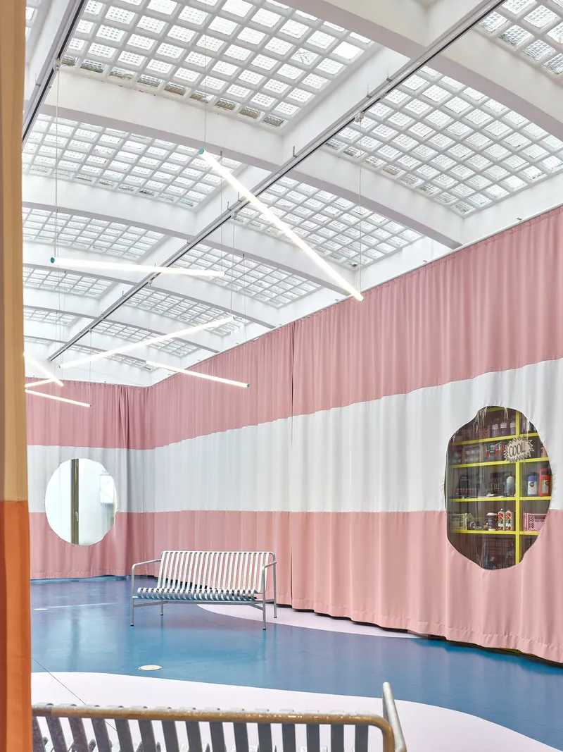 Oval cutouts in pink and white striped fabric walls reveal bookshelves under a translucent grid ceiling