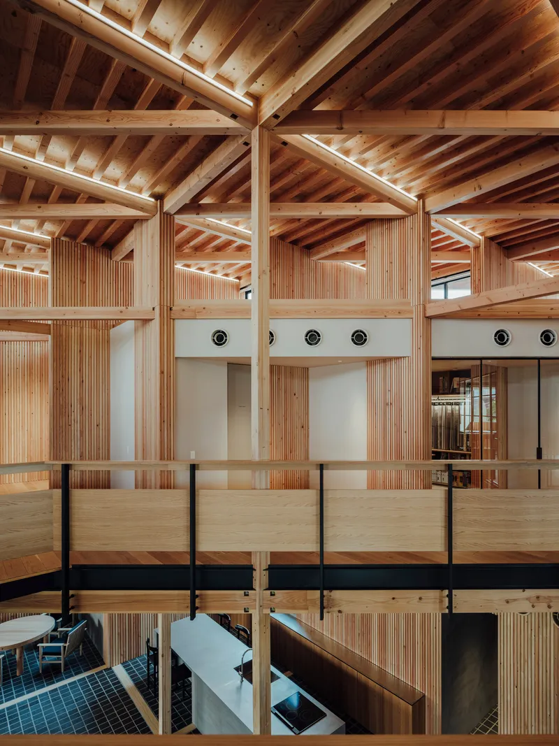 Upper-level gallery overlooking void with exposed timber structure, plywood balustrade, and circular ceiling vents in clerestory wall