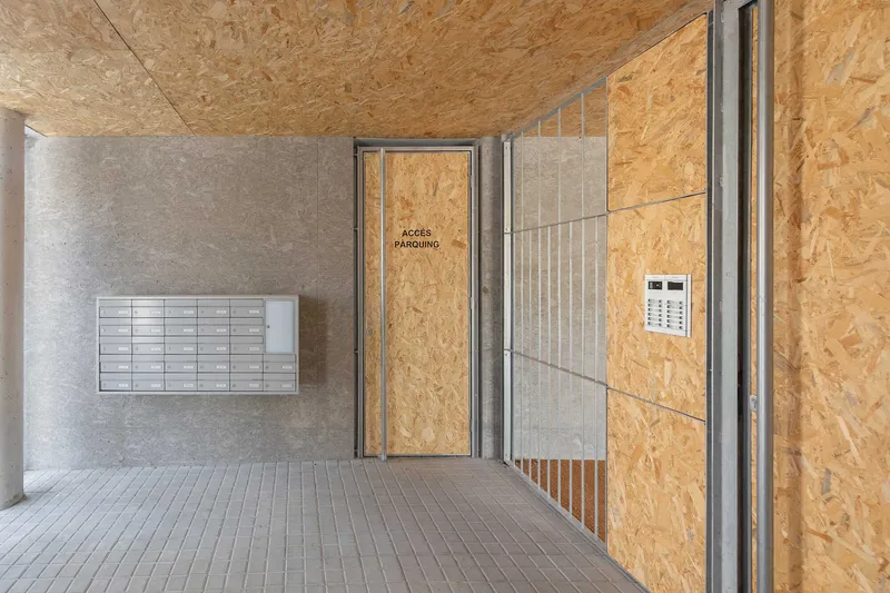 Lobby space with wall-mounted mailboxes, oriented strand board panels and corrugated metal partition