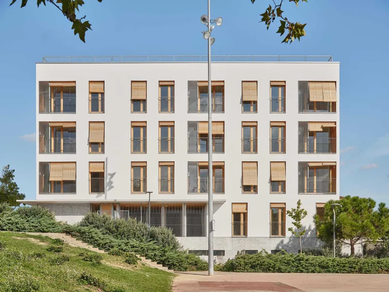 White facade with recessed timber balconies framed by trees under a clear blue sky
