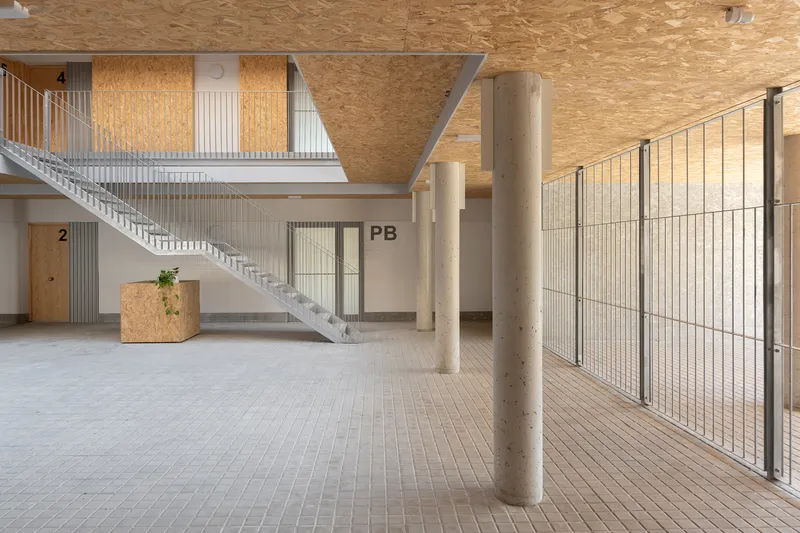 Ground floor lobby with exposed concrete columns and wire mesh bicycle storage beneath plywood ceiling