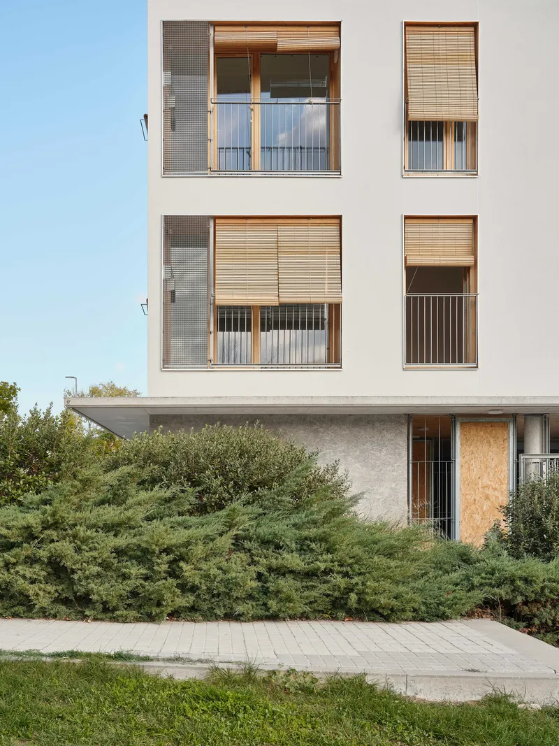 White facade with timber-framed balconies and woven reed sun shades above low shrubs