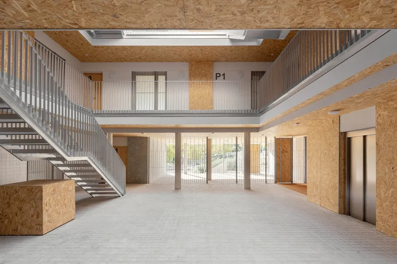 Double-height lobby with oriented strand board walls, metal railings and a central skylight