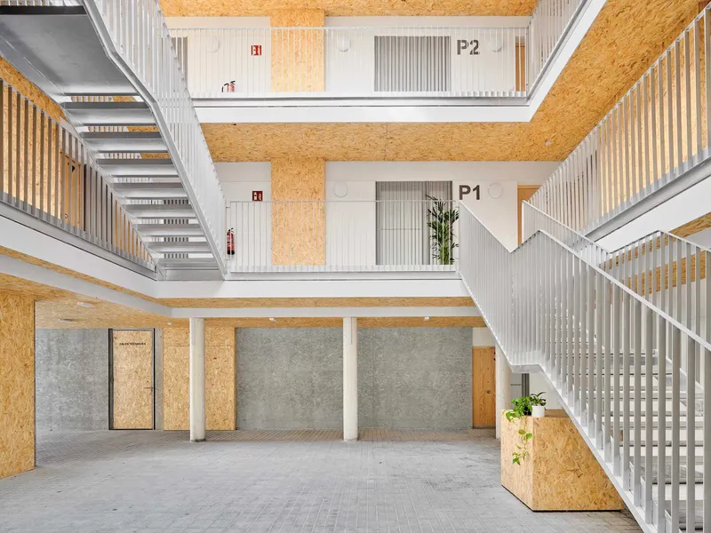 Multi-level atrium with oriented strand board walls, white slatted balustrades, and numbered unit doors