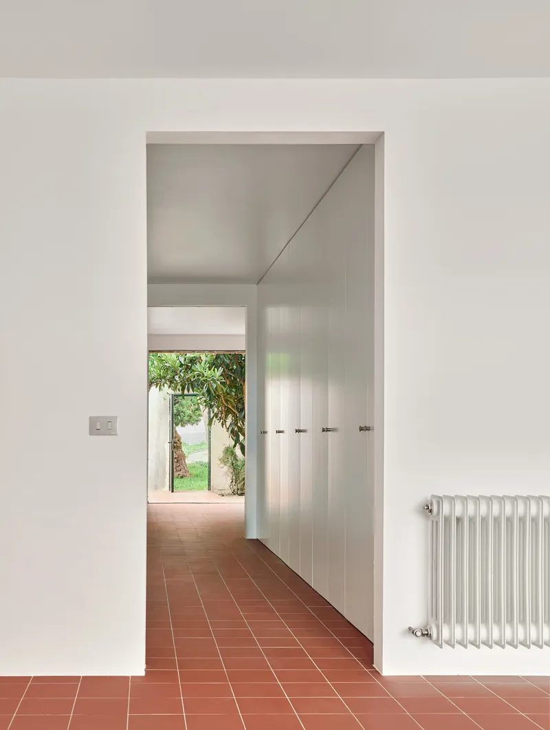 Interior hallway with terracotta tile floor and white radiator leading toward small window framing garden