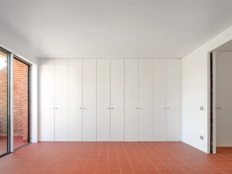 Room with full-height white storage cabinets and terracotta tile floor overlooking brick courtyard through glazing