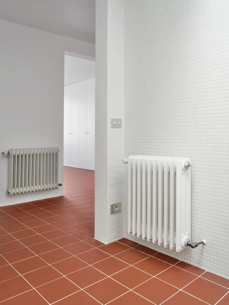 Interior hallway with white mosaic tile wall and terracotta floor tiles with column-style radiators
