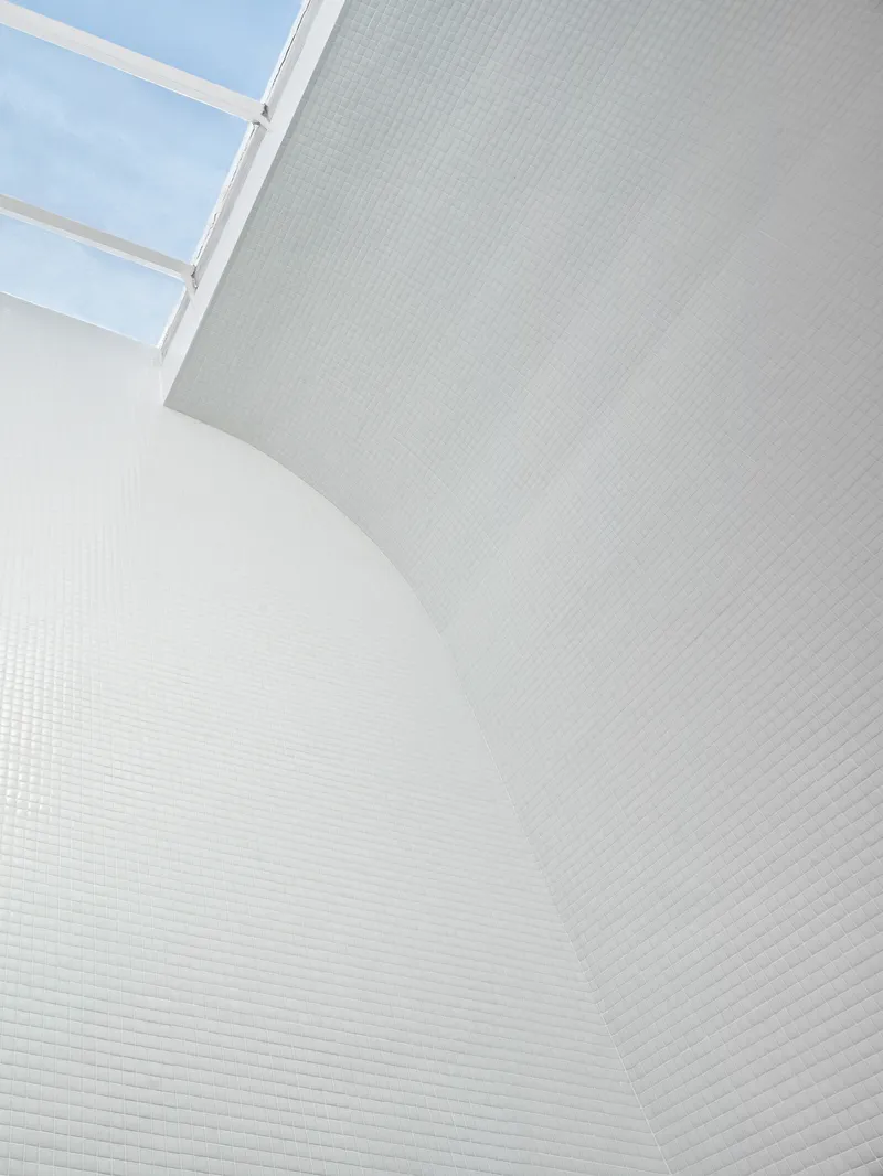 Curved white mosaic tile wall rising to a skylight under blue sky