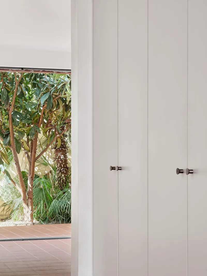 Floor-to-ceiling white storage cabinets with bronze knobs beside garden view window