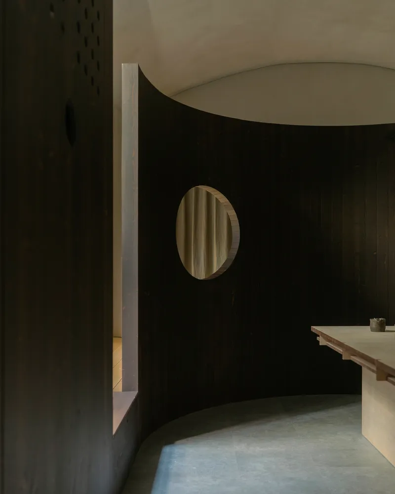 Curved partition wall with circular window reflecting curtains, meeting white plastered wall at corner in shadow