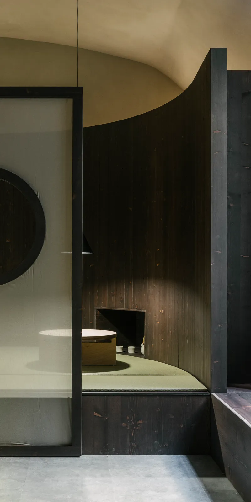 Glass partition framing a curved dark timber wall with built-in seating under vaulted ceiling