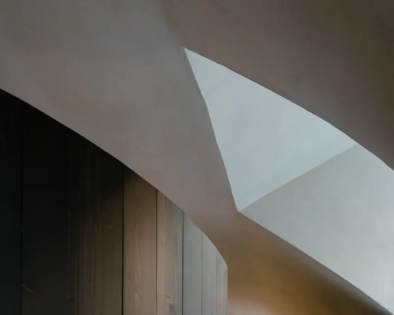 Triangular skylight piercing white plaster ceiling above dark timber wall paneling