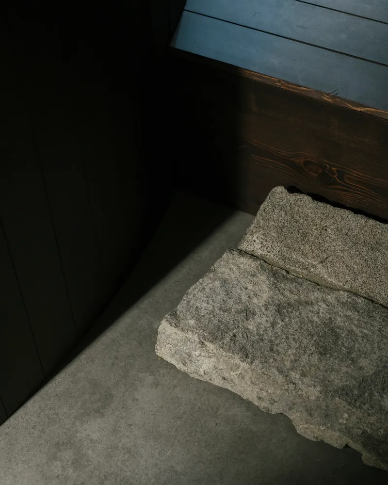 Grey concrete floor meeting a rough stone block and dark timber wall in soft daylight