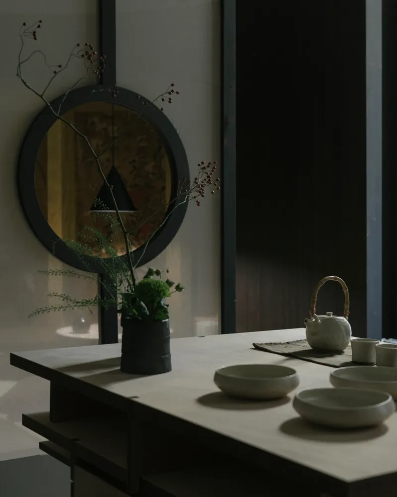 White countertop with ceramic tea set and dried branches reflected in a round mirror