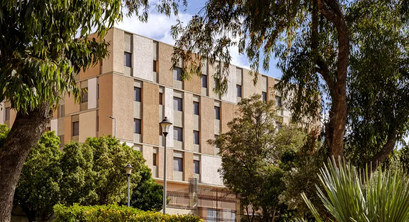 Residential tower with gridded facade seen through foreground eucalyptus branches and established trees