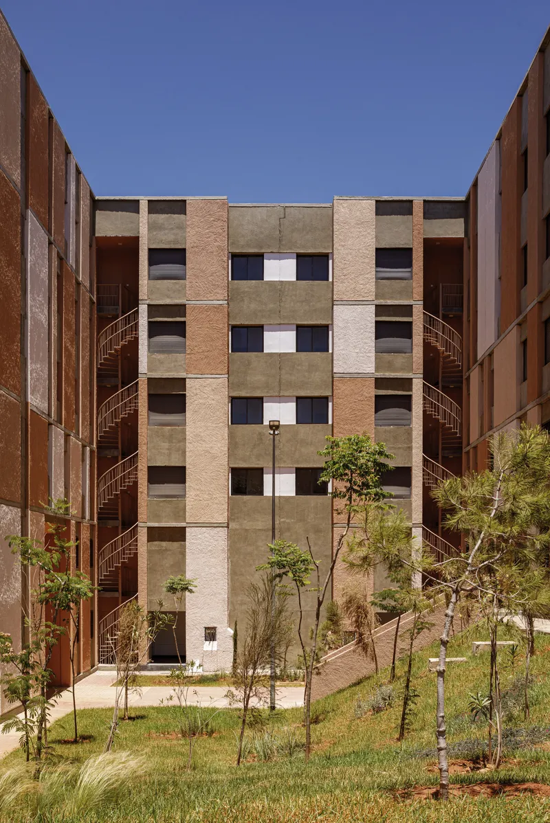 Symmetrical courtyard view with flanking staircases, central block facade, and young trees in planted lawn