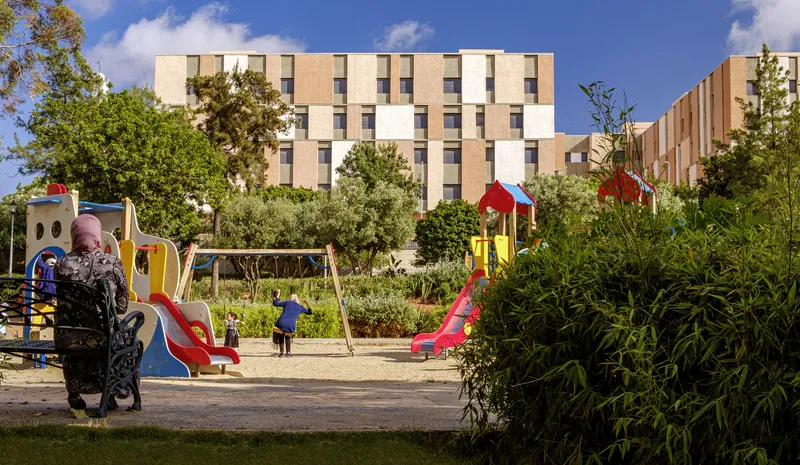 Children's playground with colorful equipment in a planted courtyard fronting a multistory residential block