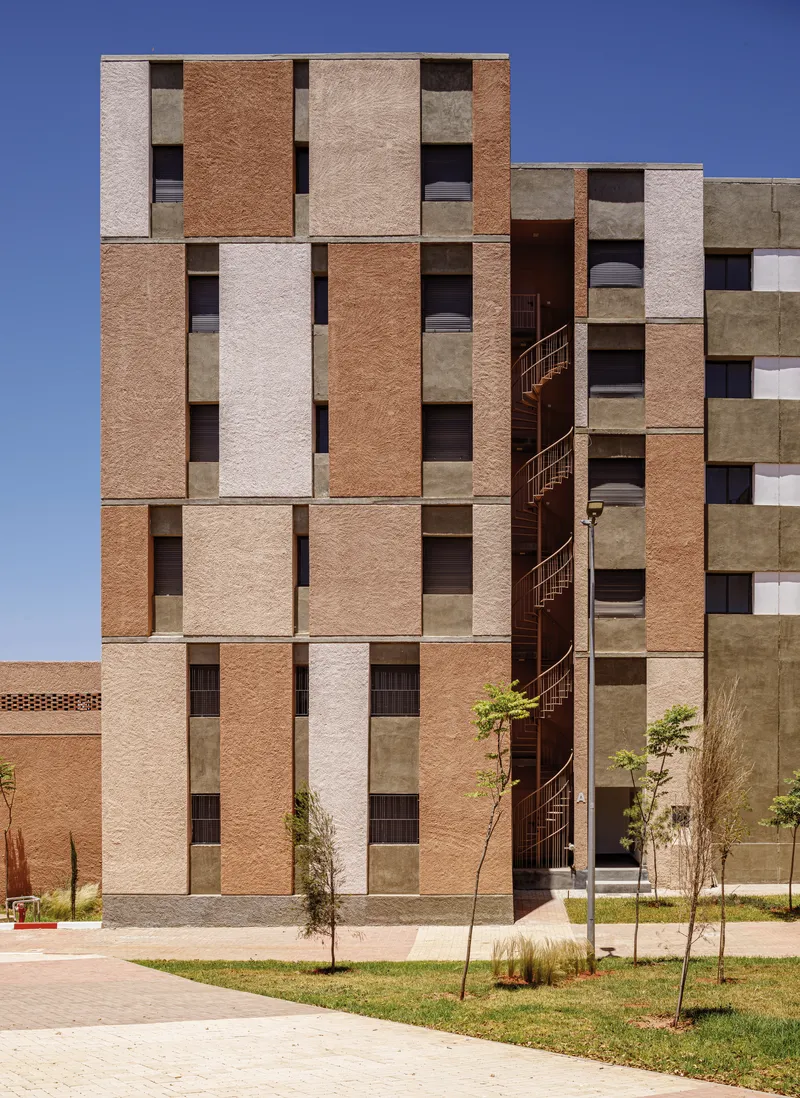 Facade of alternating terracotta and cream panels with exposed metal staircase and young saplings below