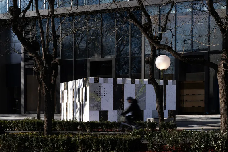 Striped marble screen wall with circular brass portal and white globe light as a cyclist passes by