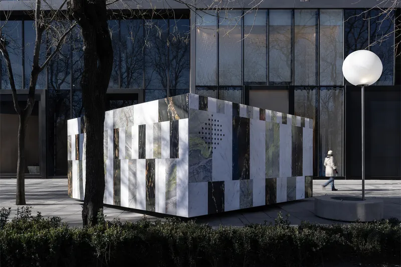 Corner view of the pavilion showing vertical marble slats against a dark glass curtain wall and pedestrian walkway