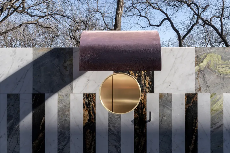 Close-up of the circular brass disc set within white marble panels beneath the copper overhang canopy
