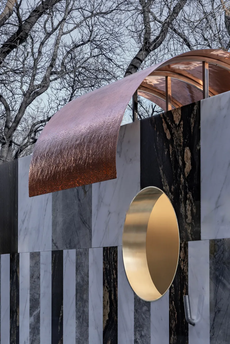 Detail of the curved copper canopy extending over the brass portal and marble facade in afternoon light