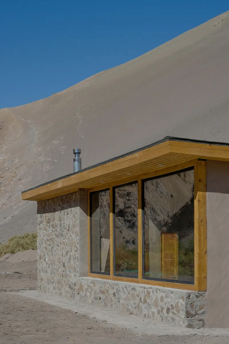 Corner glazing framed in timber with stone base wall at the foot of a sand slope