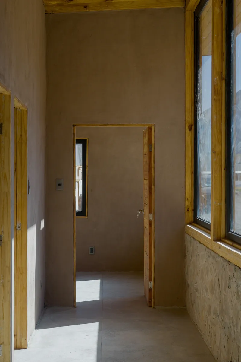 Hallway junction with timber-framed doorway and narrow vertical window casting sunlight across plastered walls