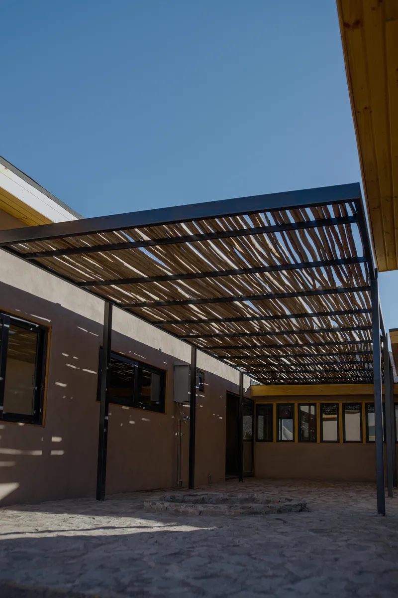 Sheltered courtyard with slatted steel overhead canopy filtering daylight onto plastered walls and stone paving