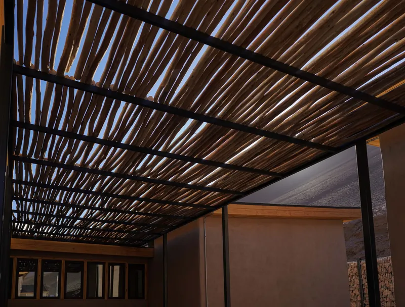 Covered outdoor space with slatted timber roof supported by black steel beams at dusk