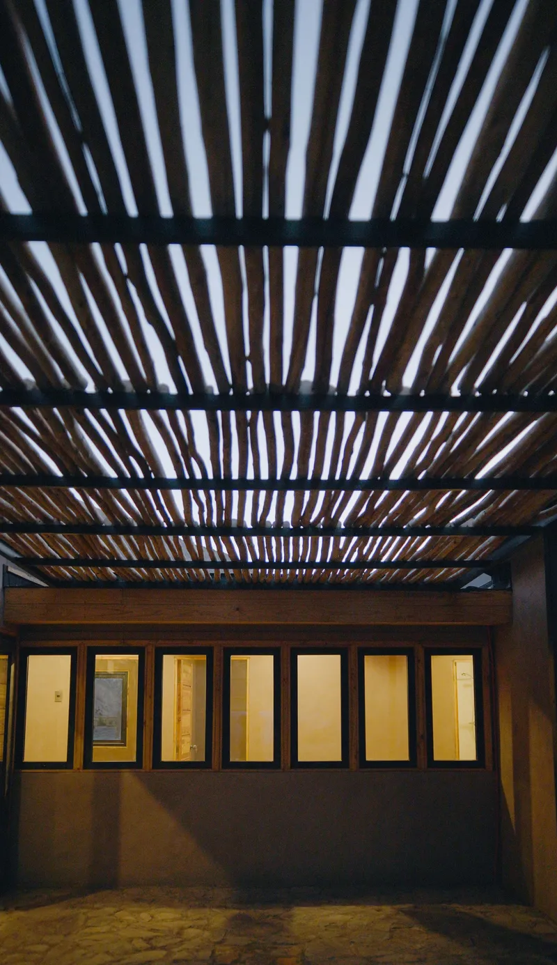 Courtyard view of timber pergola above illuminated glazed doors in the evening