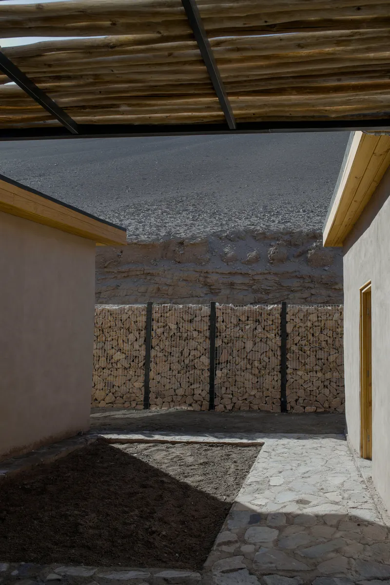 Interior courtyard with stone-filled gabion wall and earth mound under a timber pergola