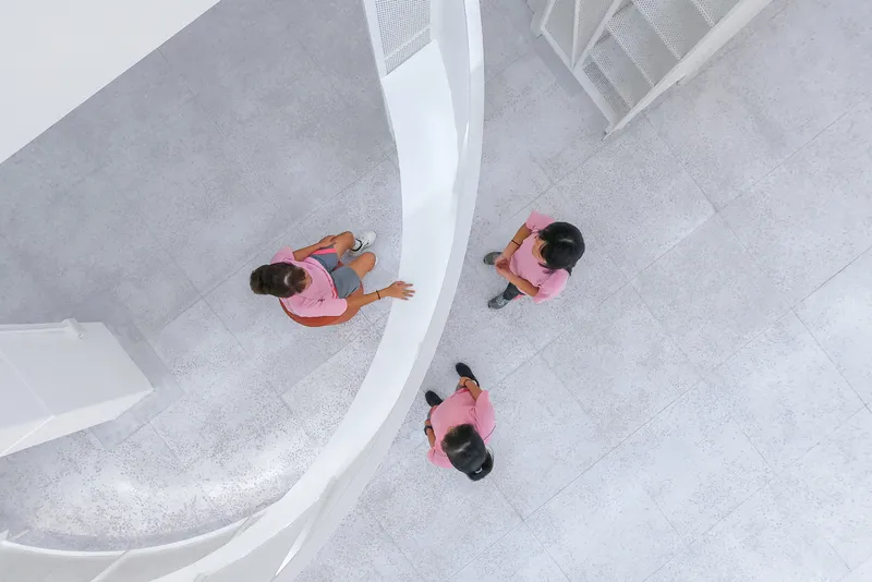 Aerial view of three visitors in pink shirts on a pale terrazzo floor beside a curved white balustrade