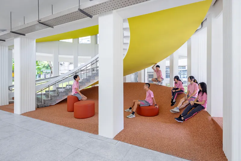 Cork terrazzo seating landscape with yellow ceiling panels and orange upholstered stools beside the staircase