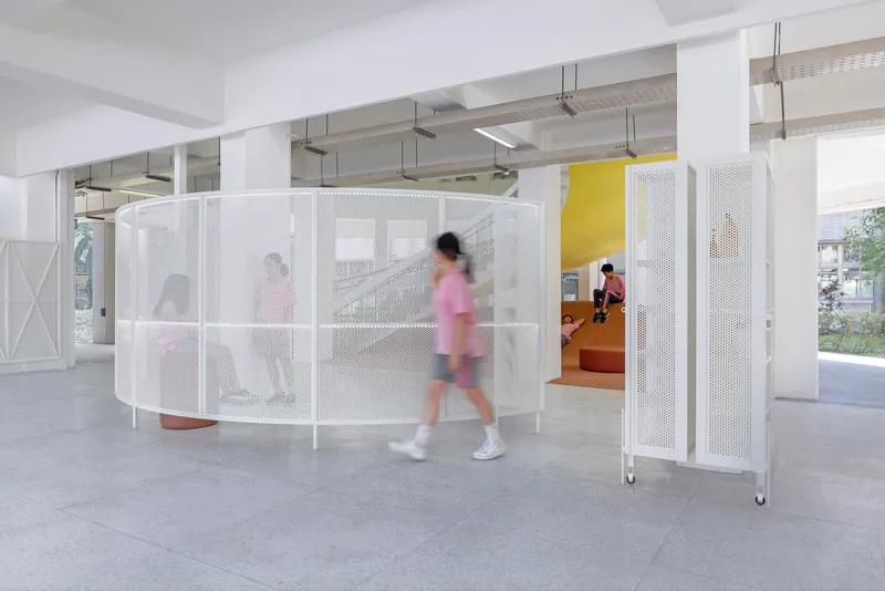 Curved perforated white metal screen enclosing the terrazzo seating area with students in motion