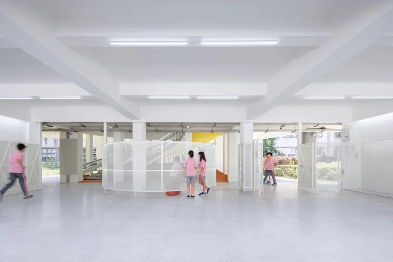 Open ground floor space with white columns and translucent partition panels as students pass through