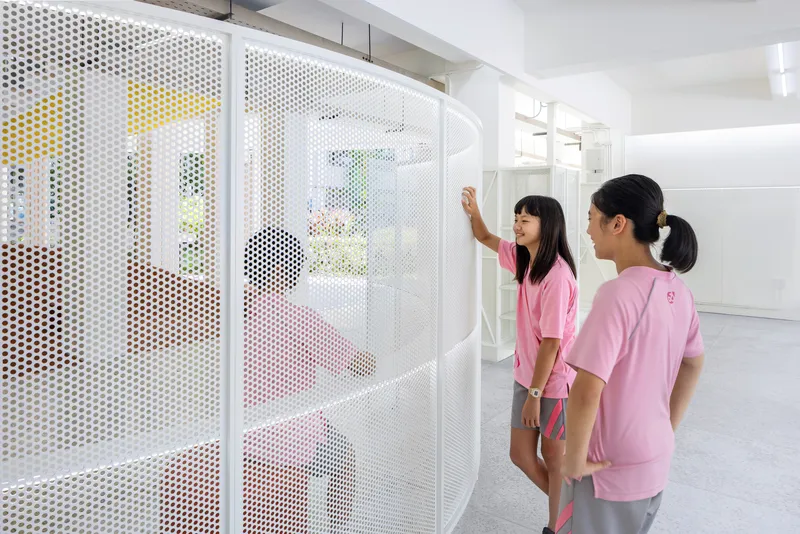 Two students examining a white perforated metal partition screen with colorful views beyond